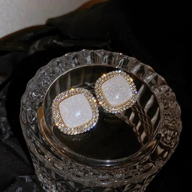 Square gold stud earrings with a white crackled stone center and pavé rhinestone border – elegant and modern statement jewelry