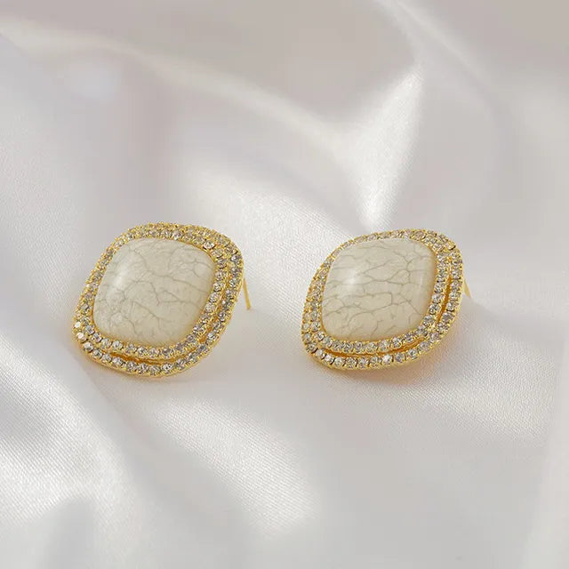 Square gold stud earrings with a white crackled stone center and pavé rhinestone border – elegant and modern statement jewelry