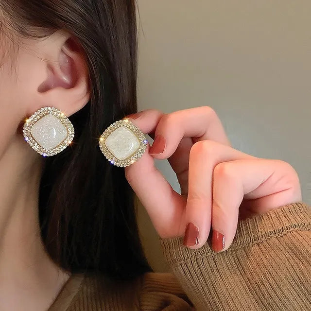 Square gold stud earrings with a white crackled stone center and pavé rhinestone border – elegant and modern statement jewelry