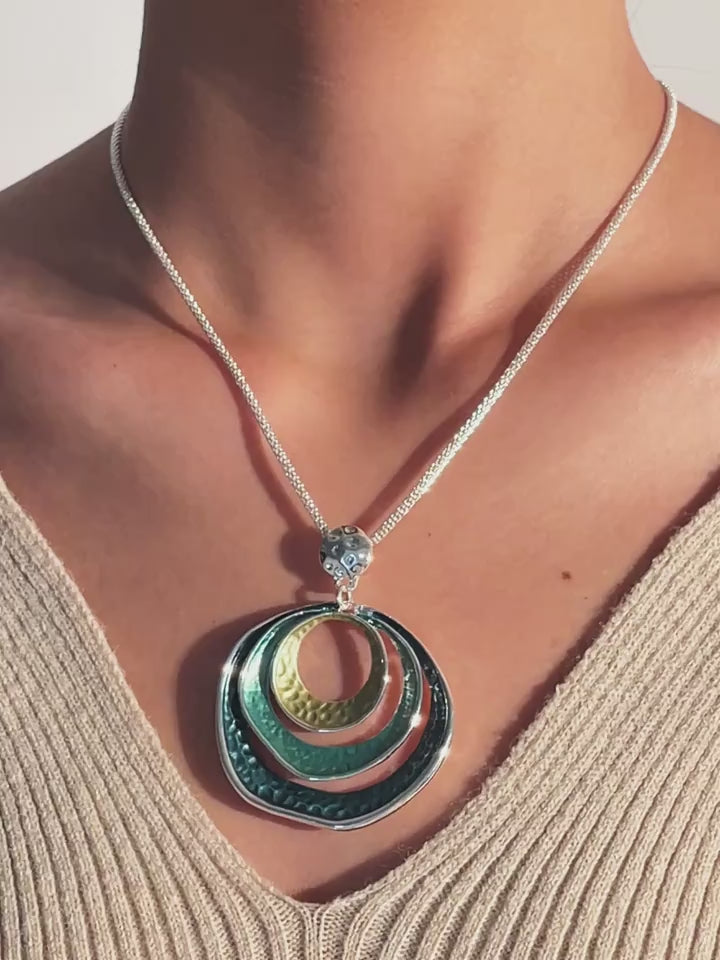 Layered concentric circle pendant necklaces in gold, bronze, and teal finishes with hammered texture design, displayed on chains.